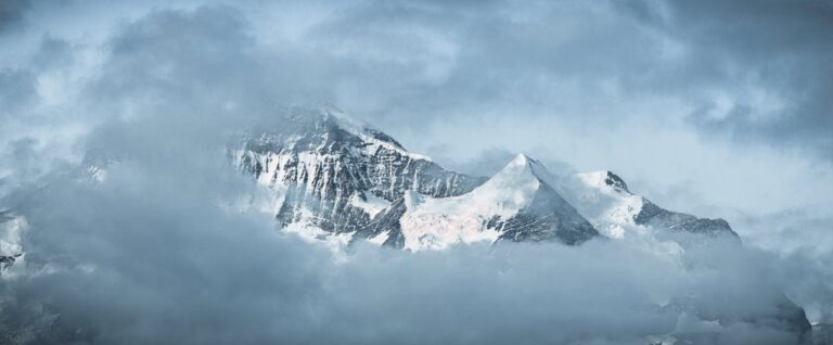 A serene view of snow-capped mountains surrounded by drifting clouds, offering a tranquil winter landscape.